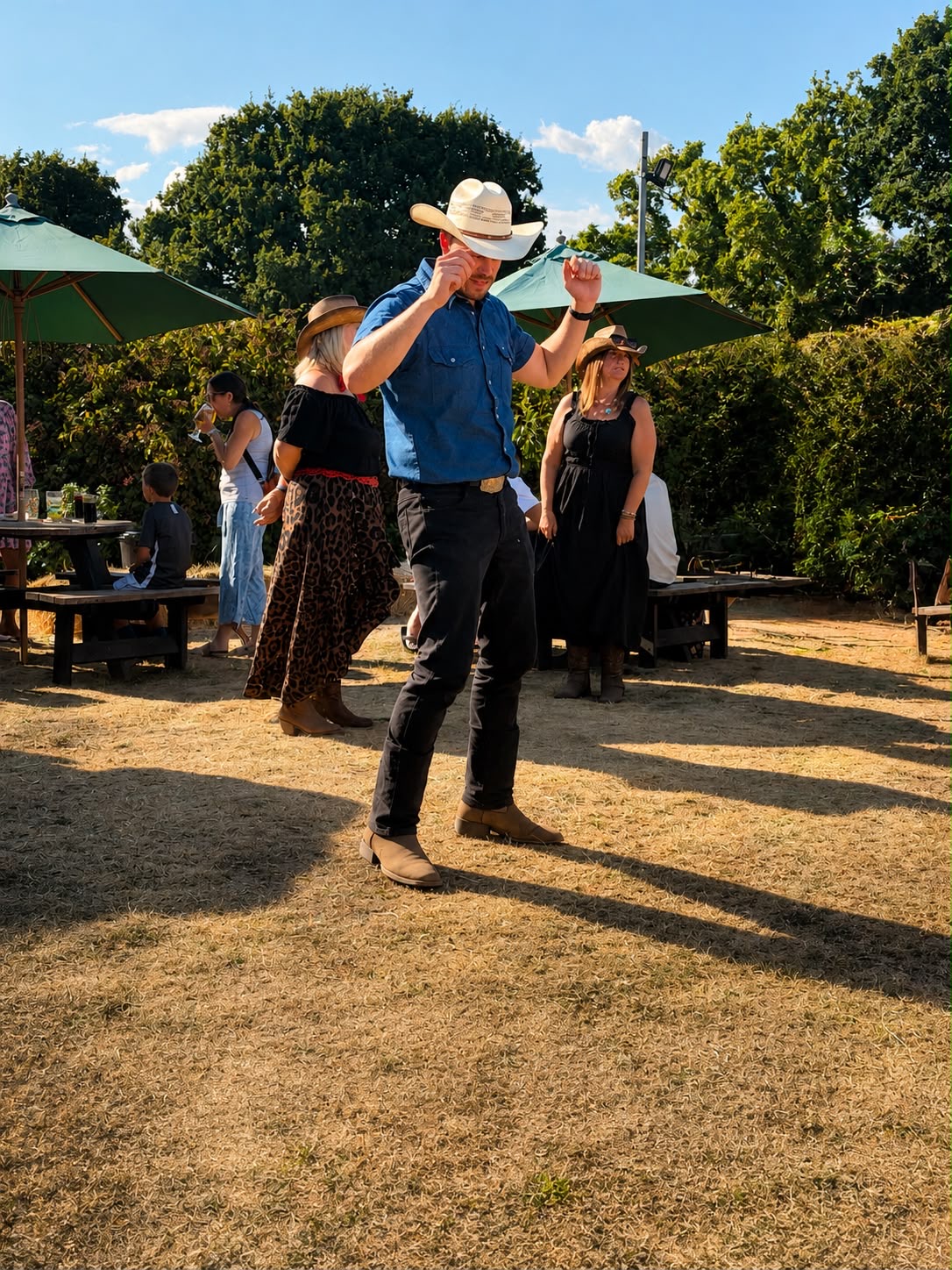 Dan Waterman in a cowboy hat leading a line dance in a sunny pub garden